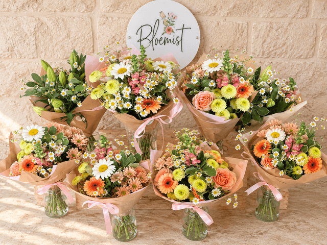 Peach, yellow and white Bloemist Club bouquets arranged beneath the florist’s sign