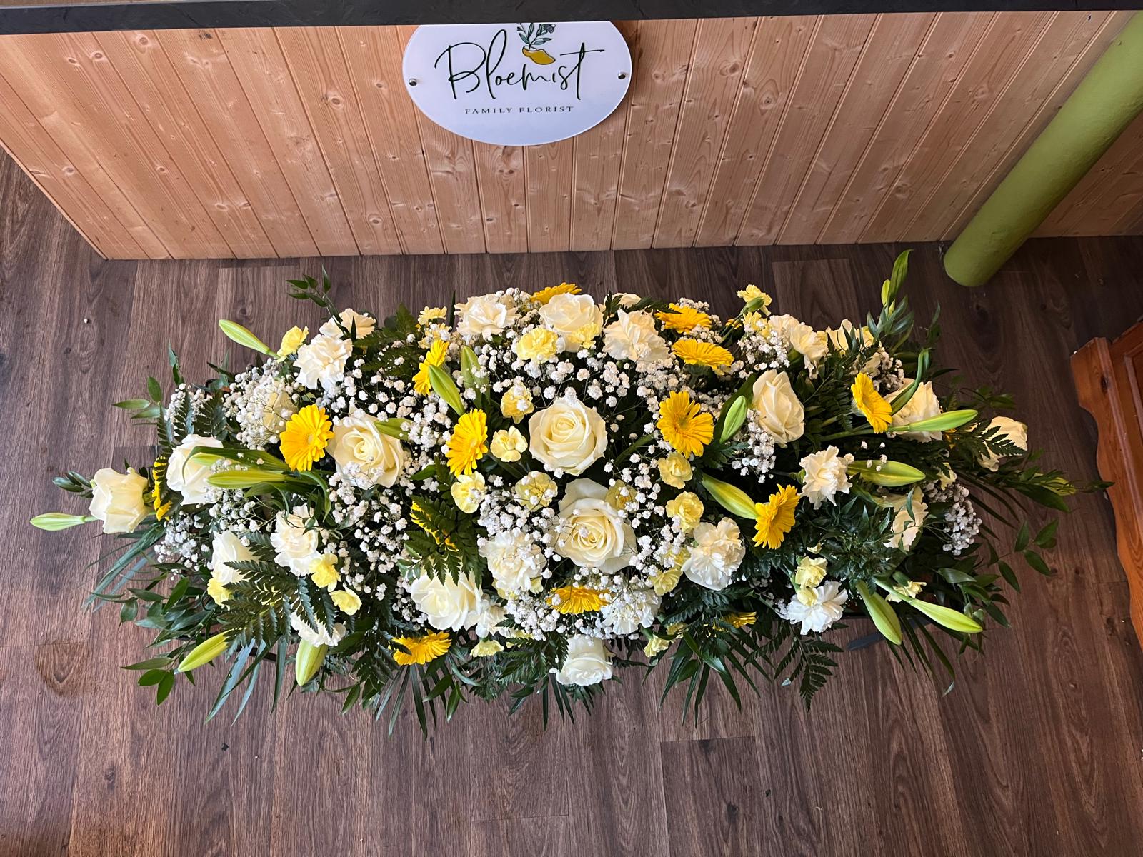 A yellow rose and white flower casket spray