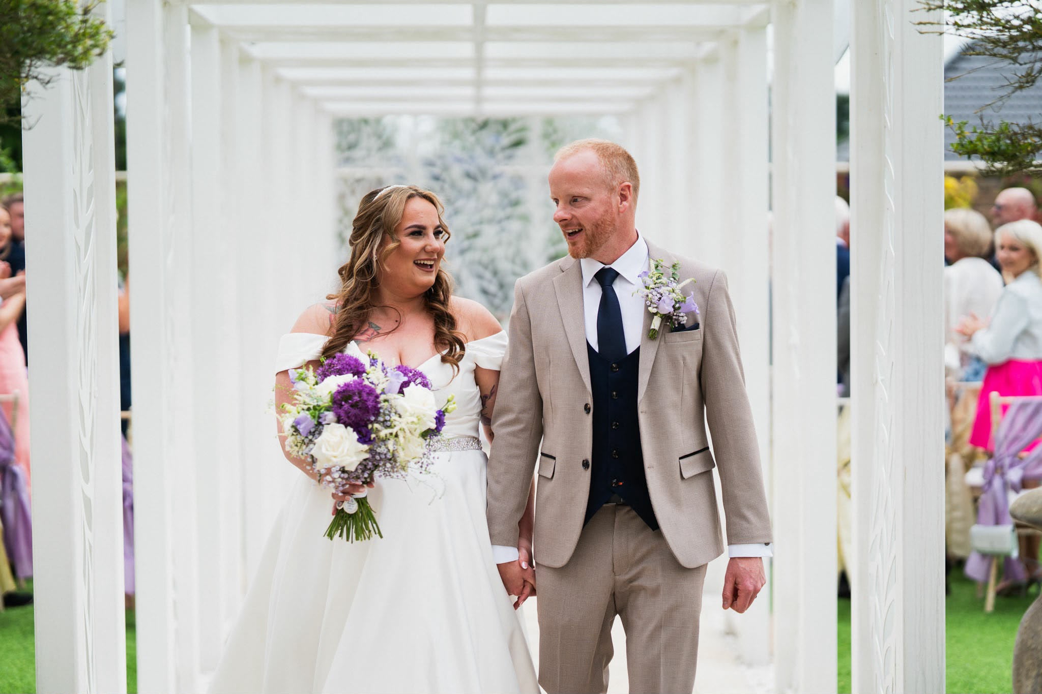 A couple walking together with a lilac and white bridal bouquet
